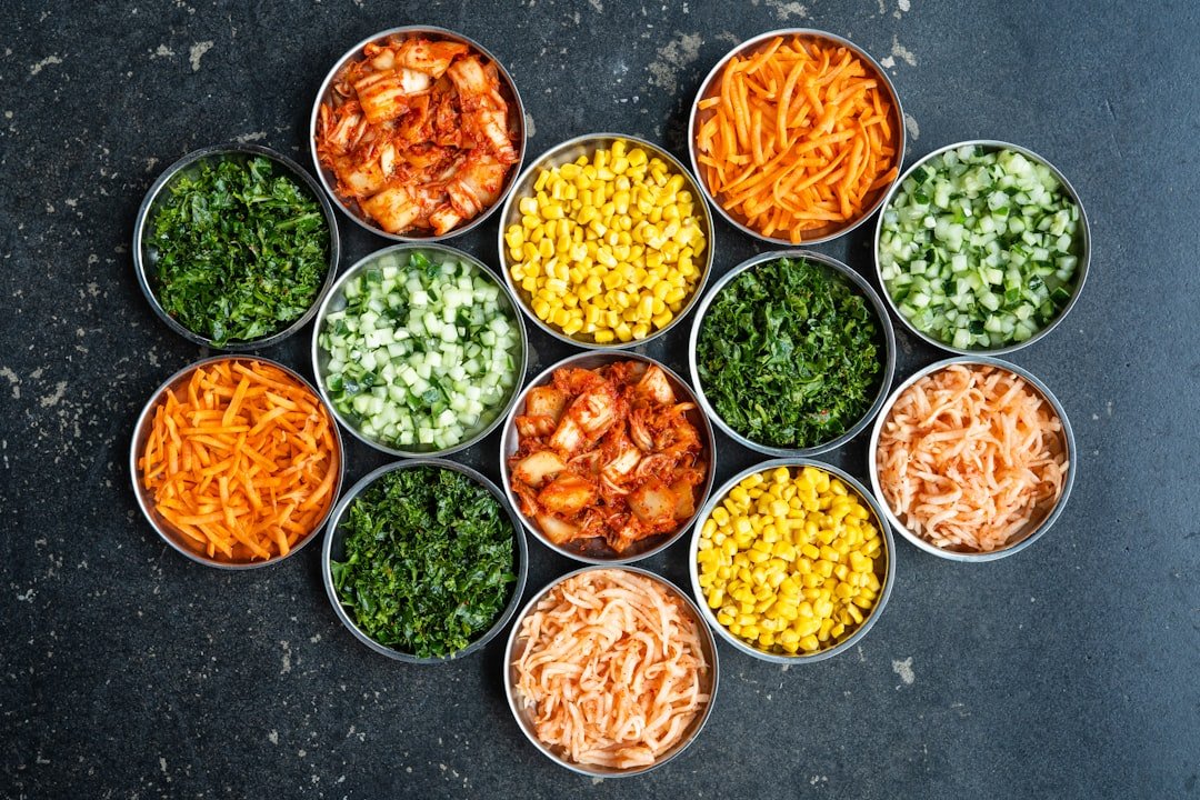Five glass meal prep containers filled with colorful lunches featuring sliced chicken, roasted vegetables, and grains arranged neatly on a kitchen counter